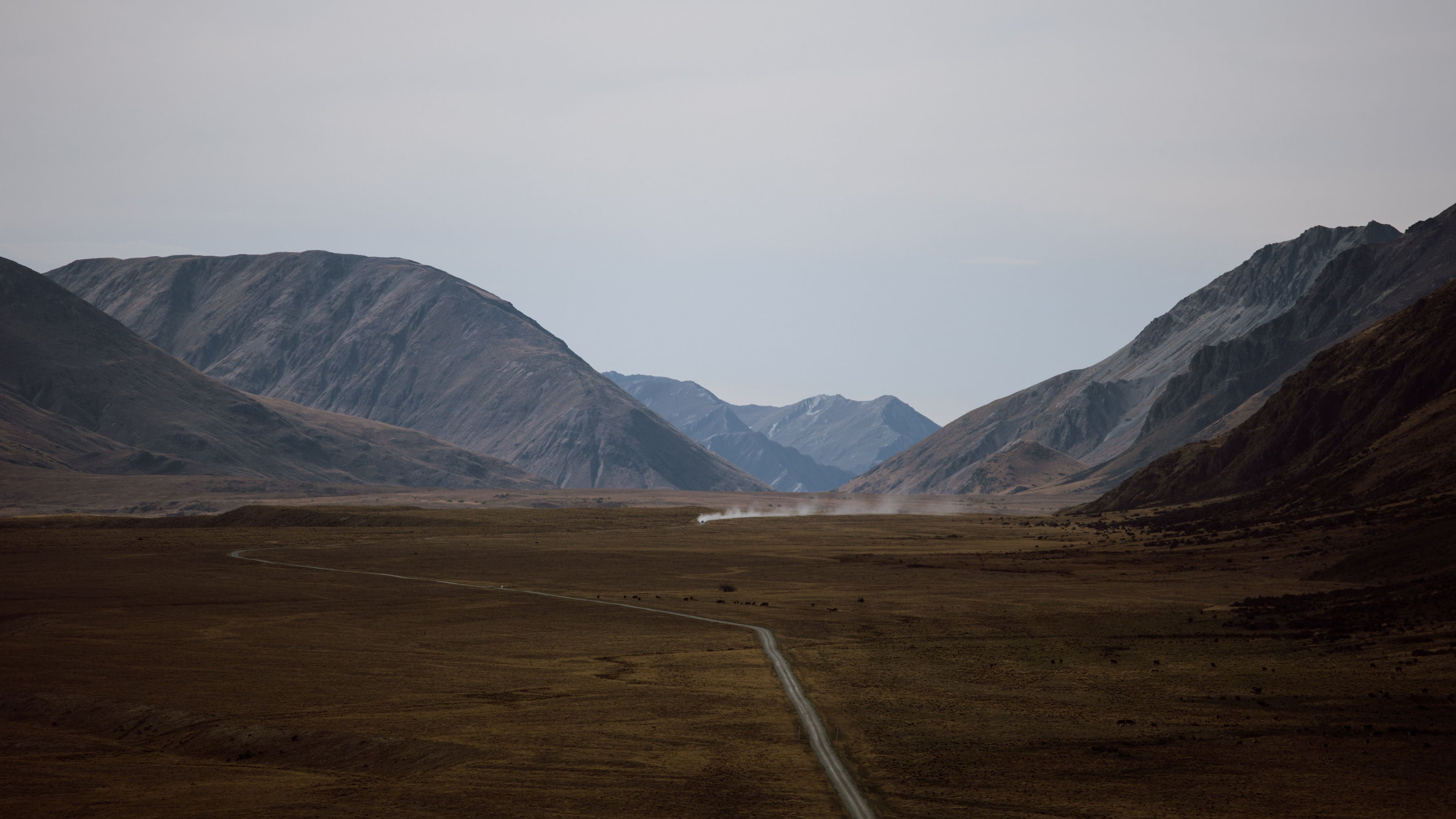 A wide landscape view of a vehicle driving up a dirt road in the valley of Mount Nicholas Station.