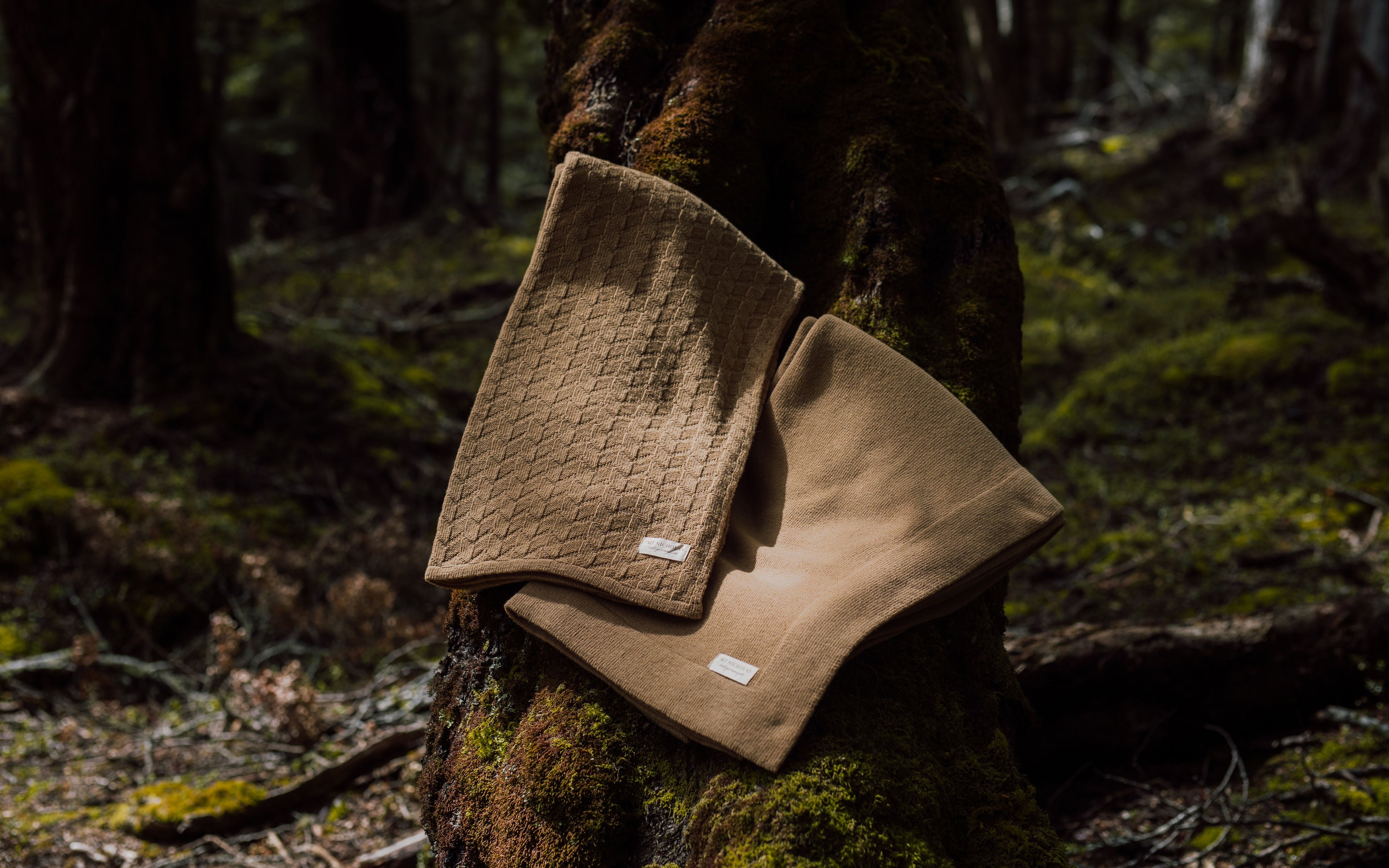 Two luxurious merino throw blankets draped over a tree trunk in the New Zealand forest.